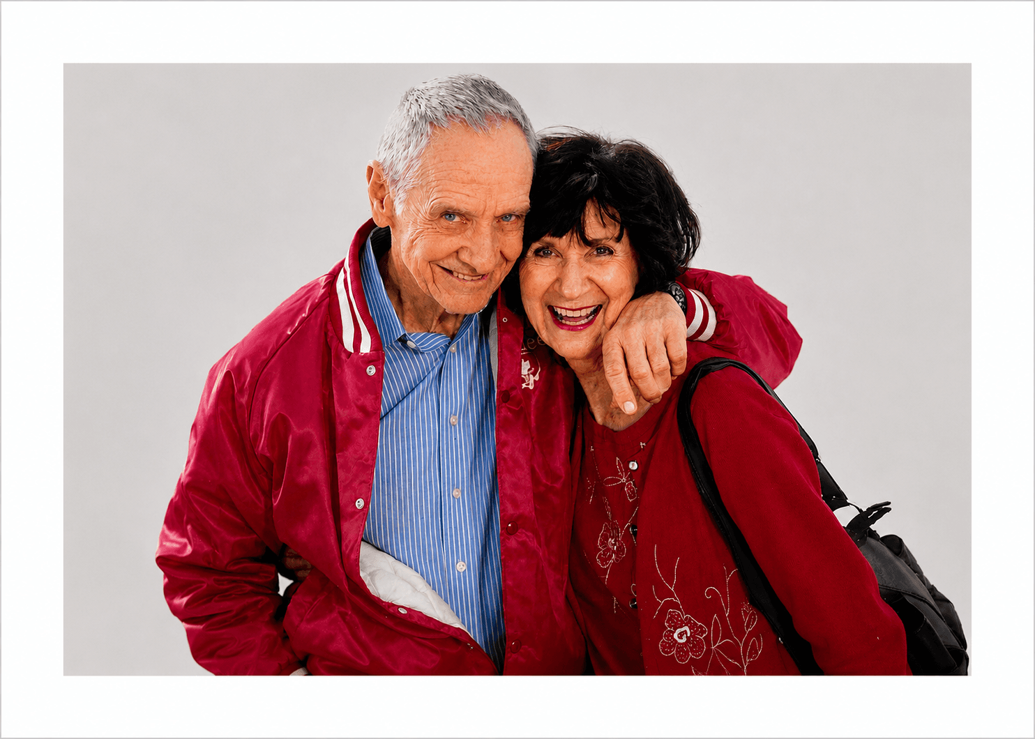 Smiling elderly man in red varsity jacket and woman in red sweater embracing.